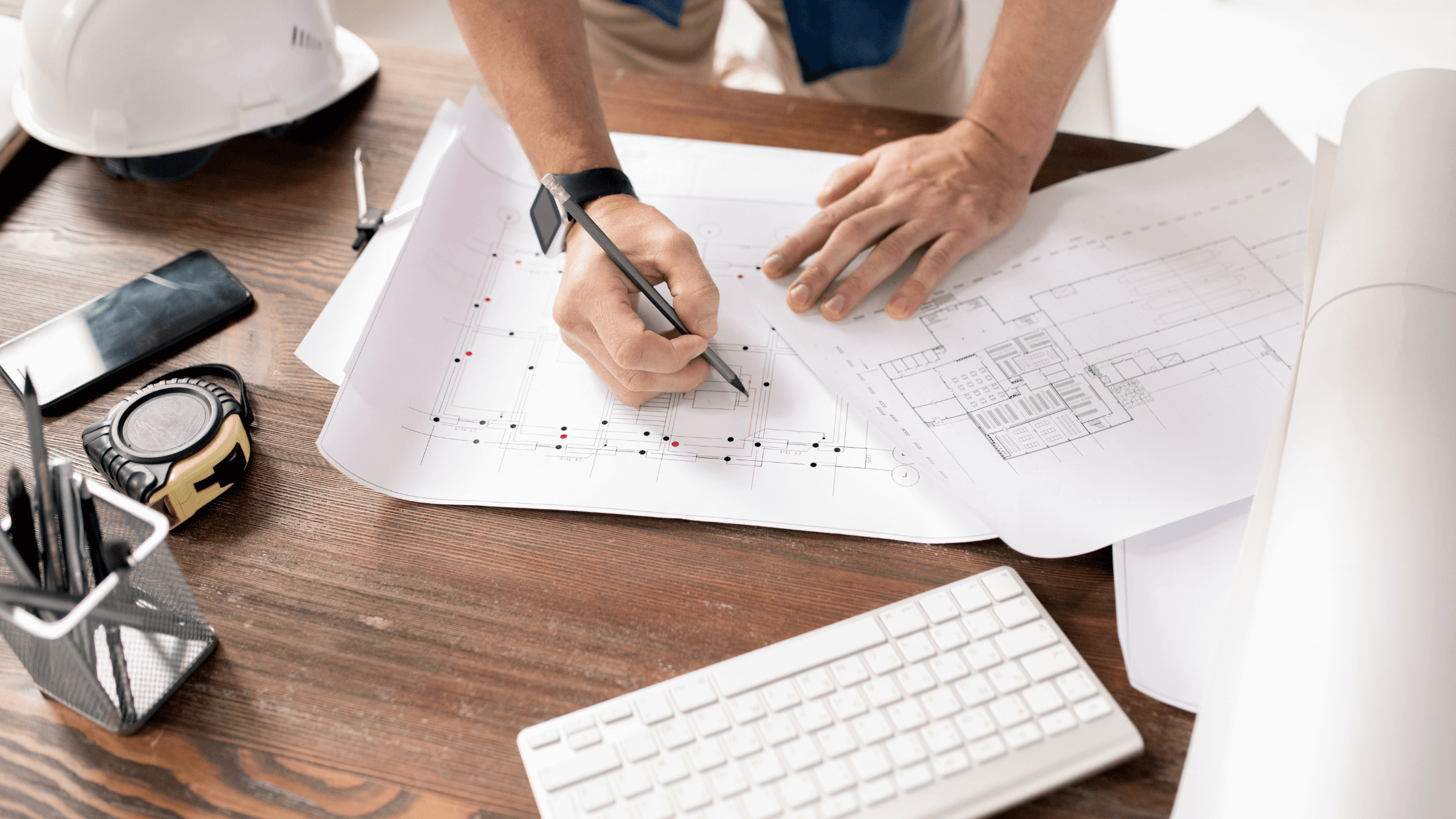 looking down on a desk with keyboard, drafts of home interior and a hand writing on drafts