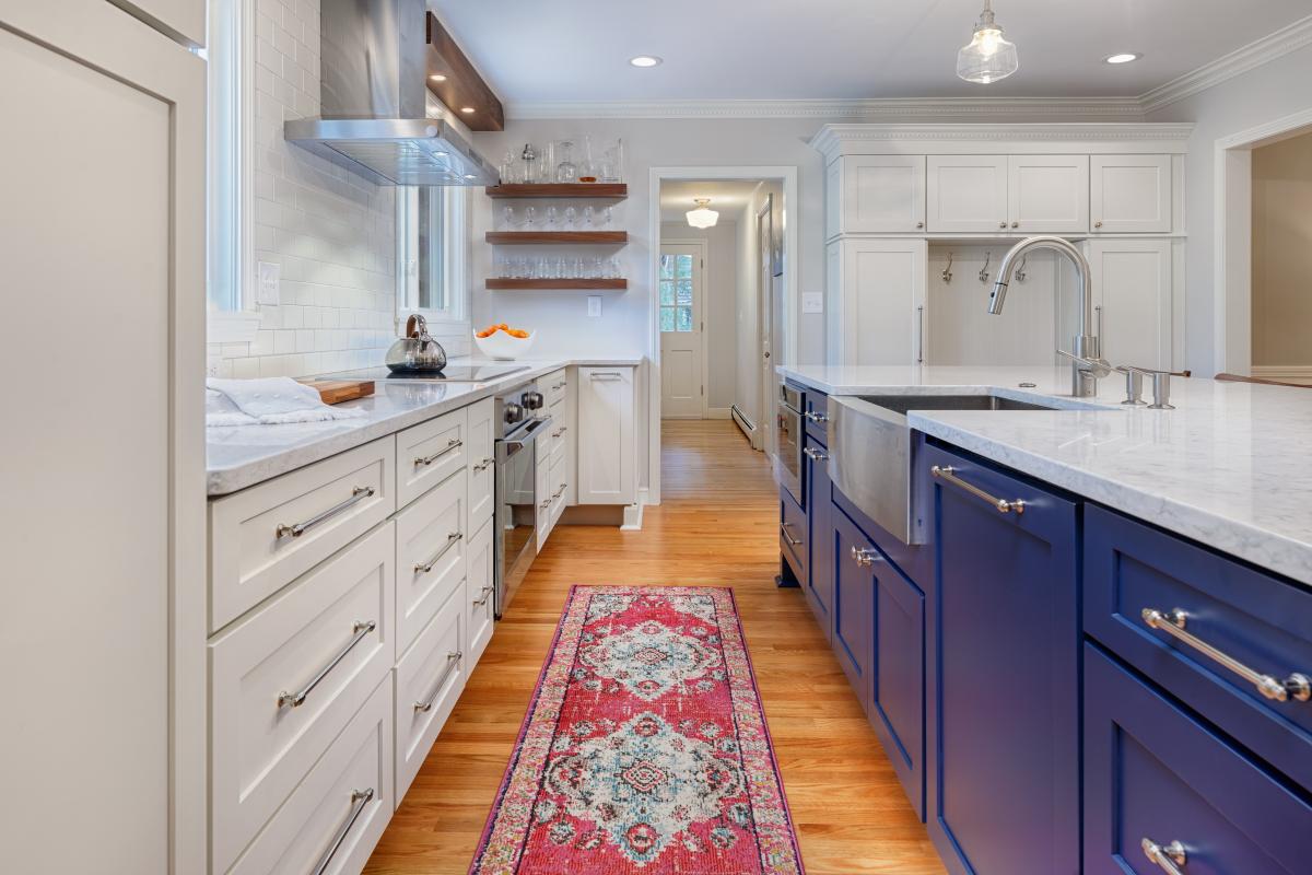 Kitchen with predominantly white cabinets. Lots of storage space and has an island with a sink and blue colored cabinets at the bottom. There's also a red rug in the middle.