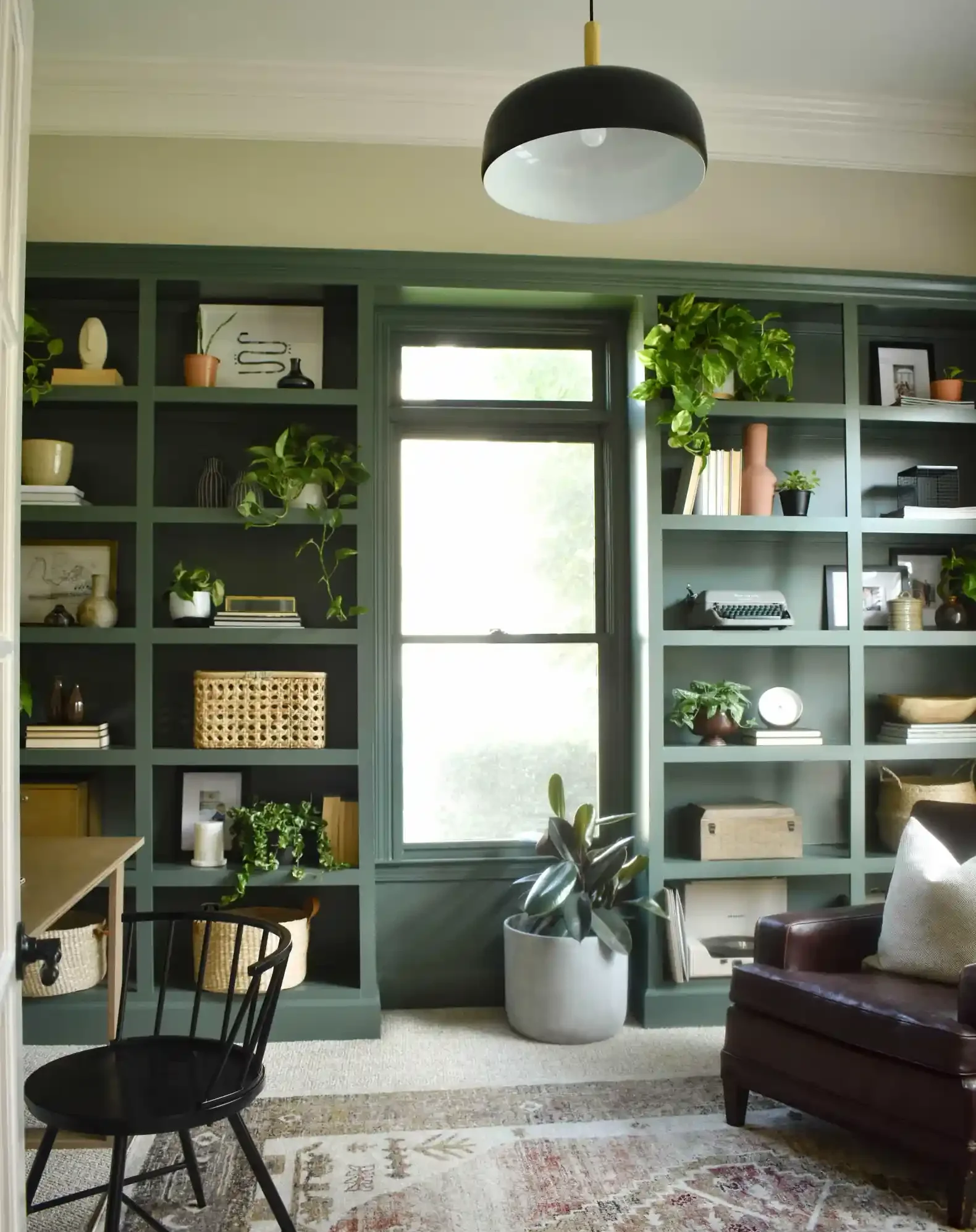 home office with green built-ins, colorful rug, black pendant light