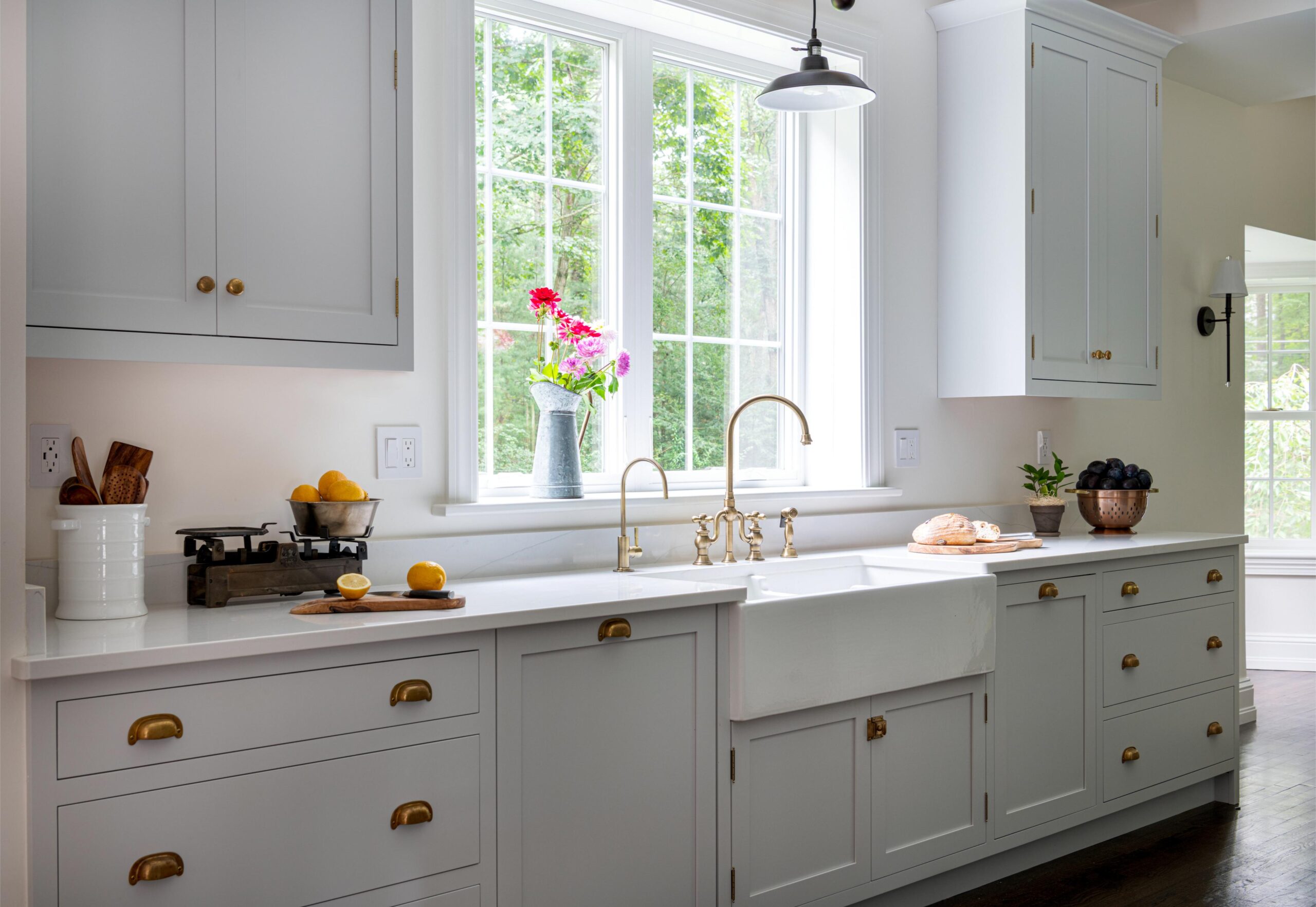 A bright kitchen with white cabinets and a white farmhouse sink. The door handles of the cabinets are gold.