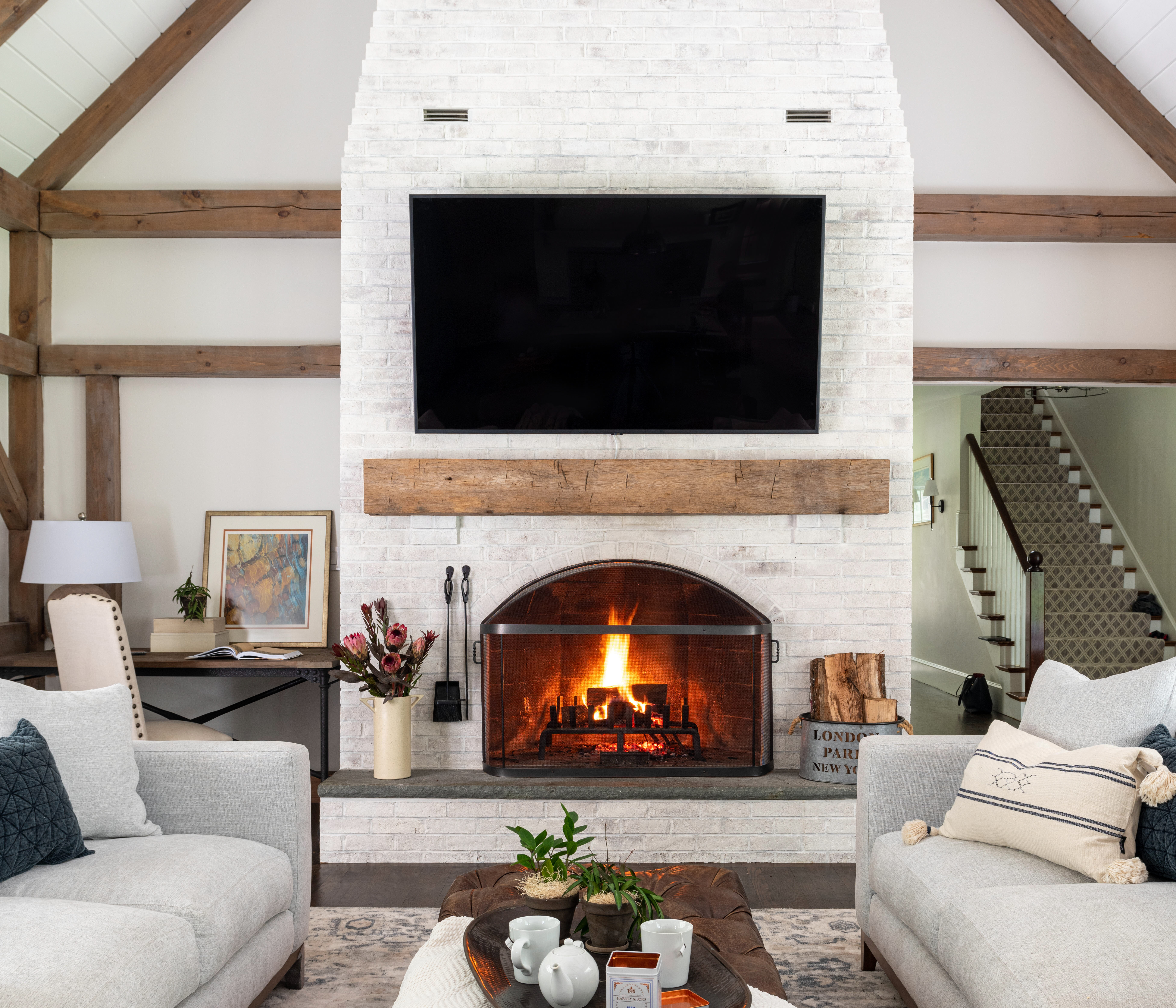 living room with high ceilings, fireplace, tv mounted above fireplace, wooden beams overhead, cream colored couches