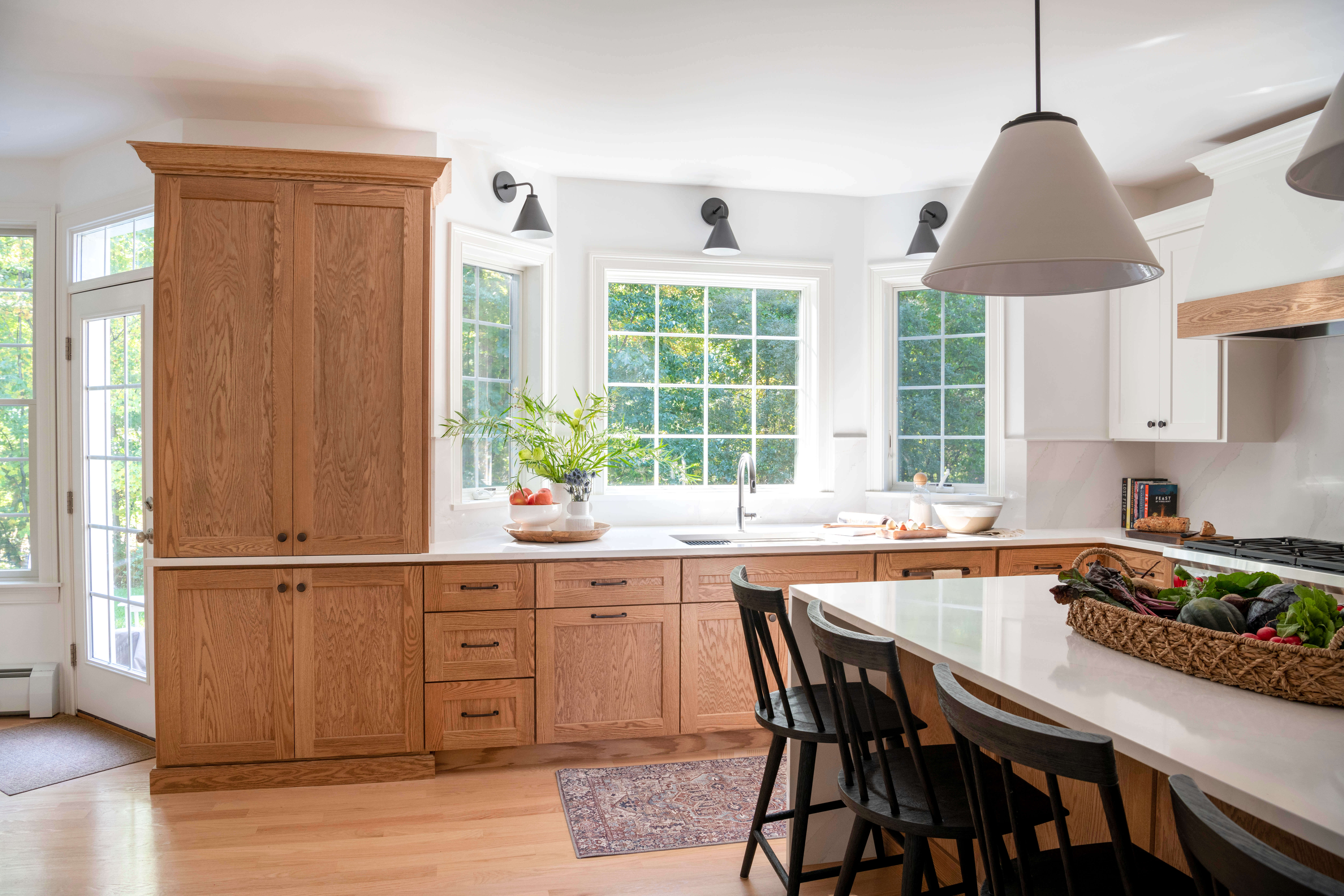 natural wood cabinetry, large white pendant light, wood flooring, black counter seating, white countertop and island