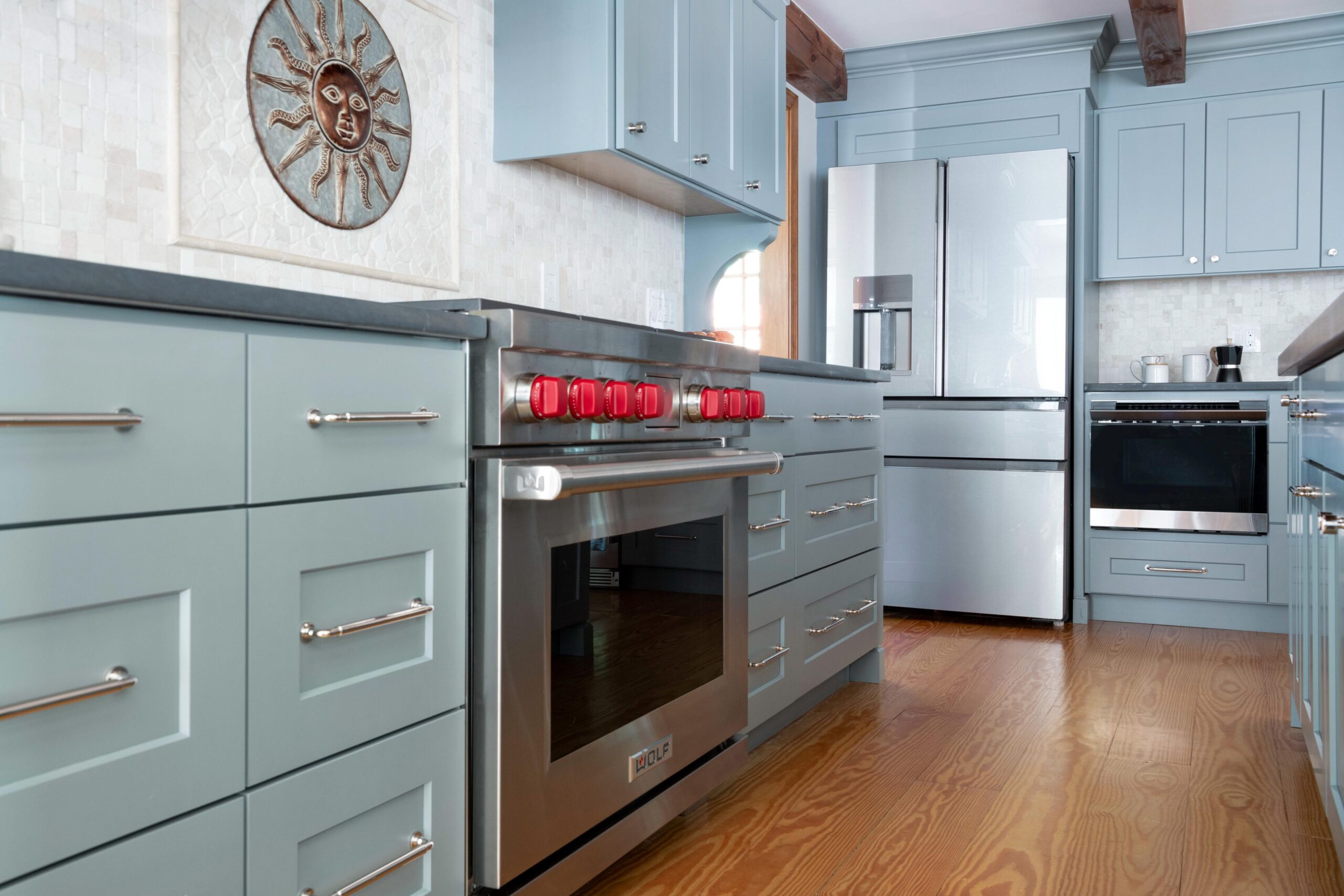 Blue cabinets line the wall of this kitchen. It has a cooking range with bright red control knobs. The two door refrigerator in this kitchen matches the color if the cabinets.