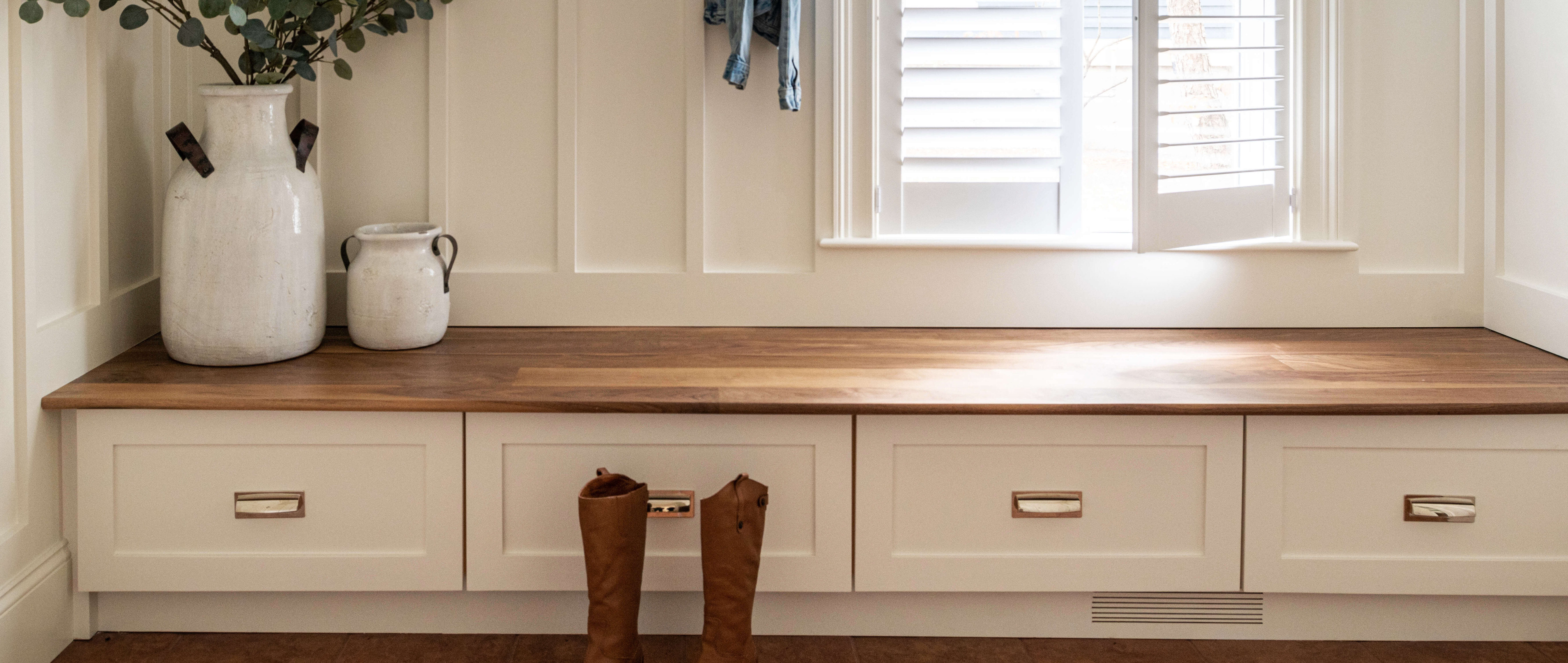 bench seat with drawers underneath, boots on the floor, flowers in a vase, open window