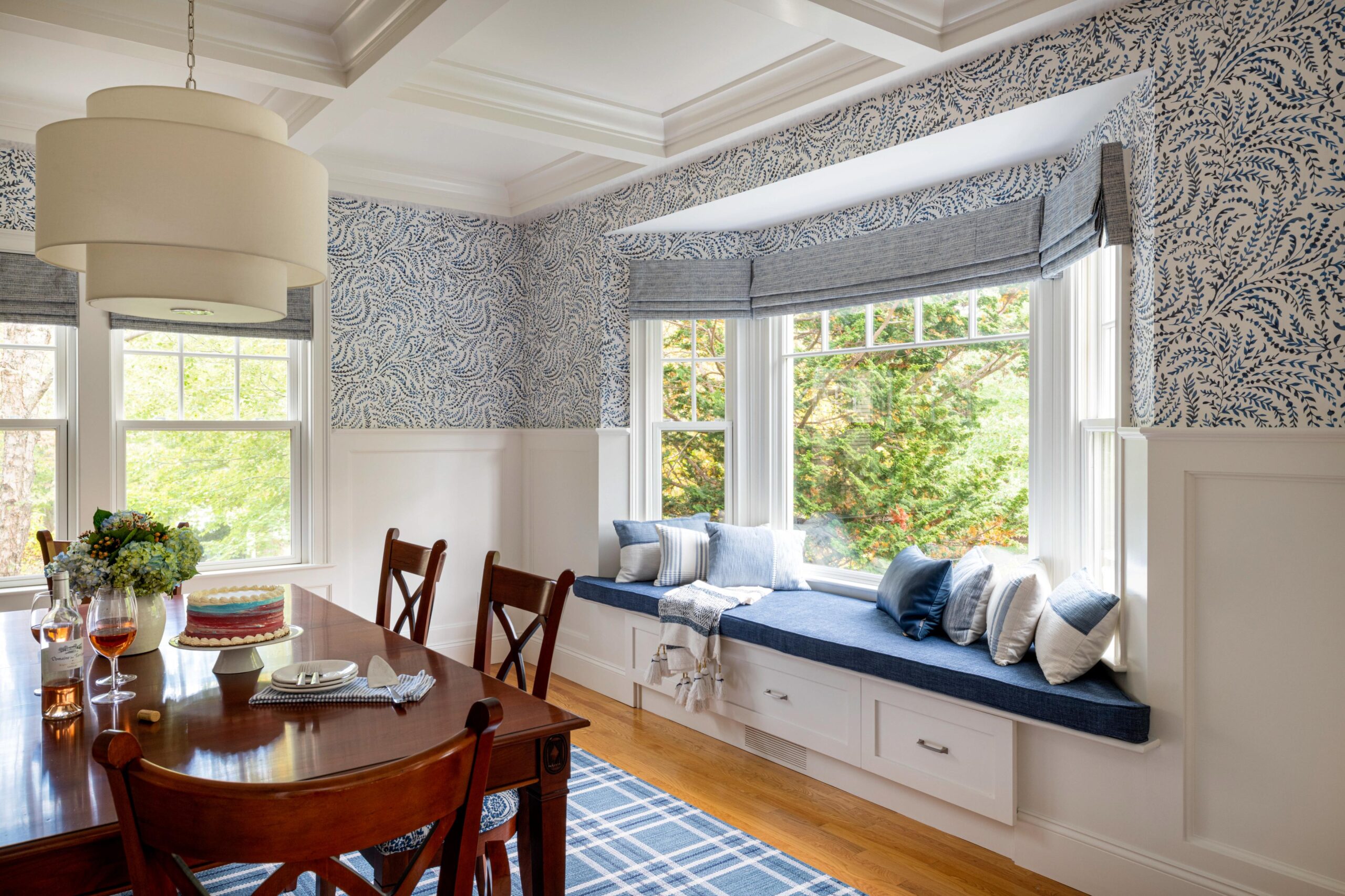 dining room with coffered ceiling, blue wallpaper, window seat, blue accent pillows