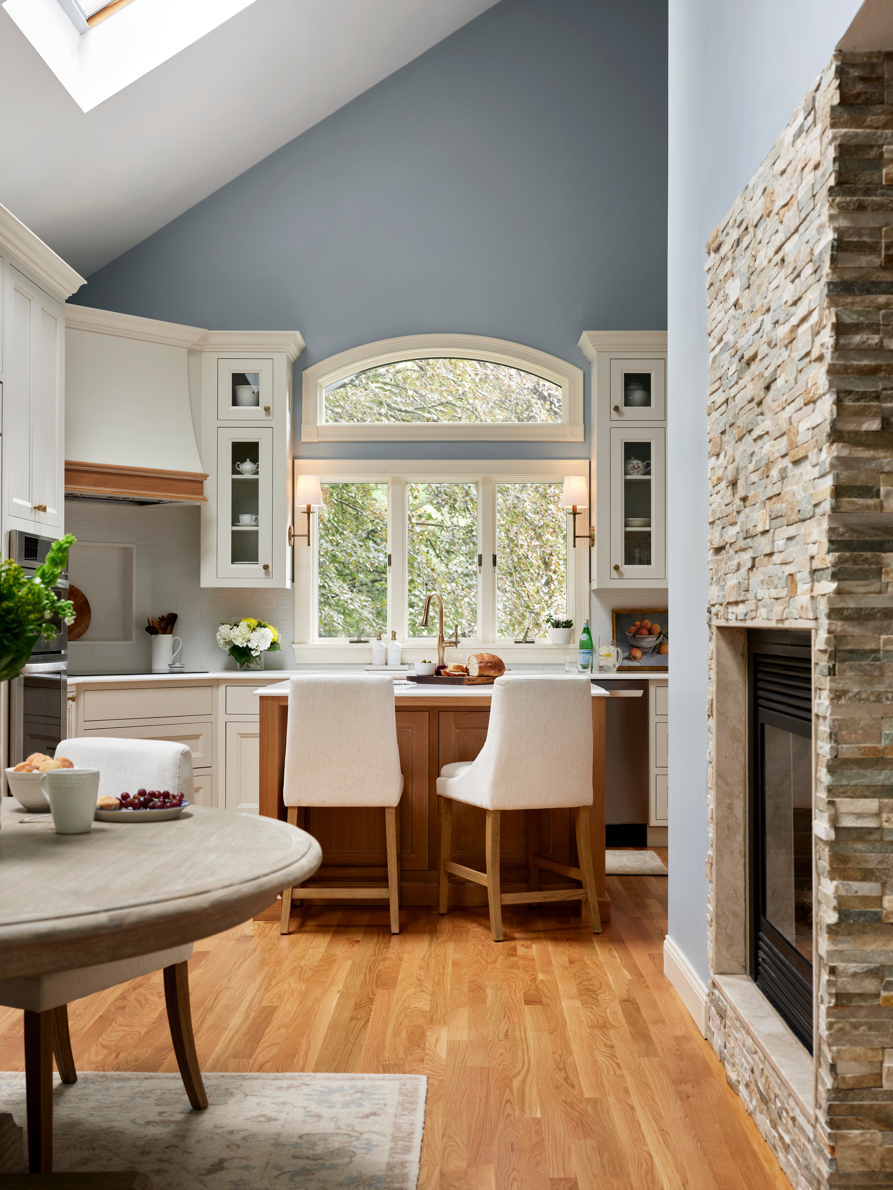 white kitchen cabinetry, blue wall paint, stone fireplace, natural wood stained island, round wood dining table