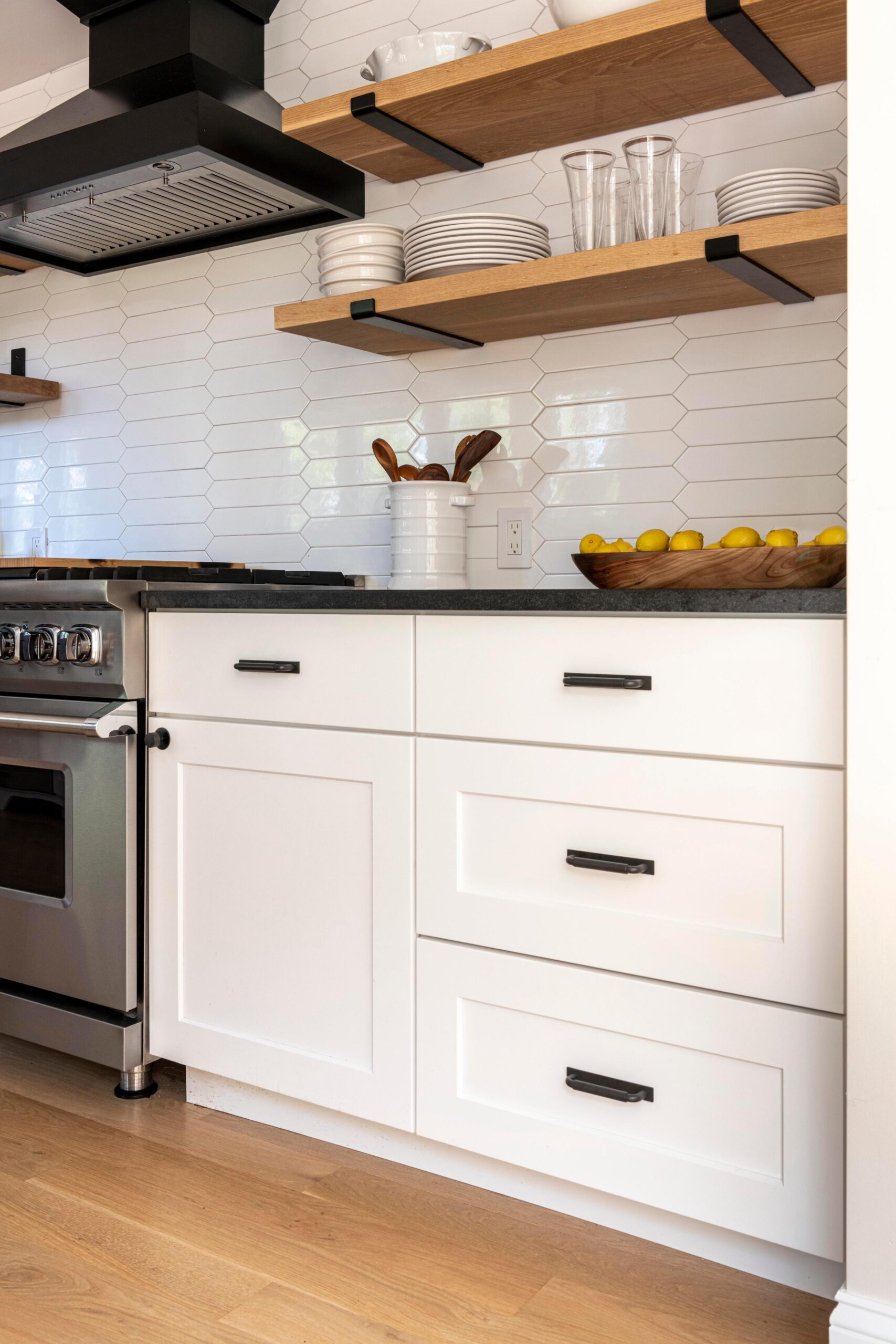White cabinets with black handles. Above are open shelves with plates, cups, and bowls.