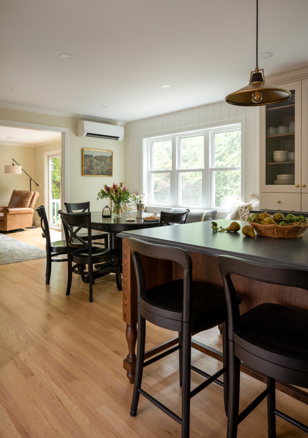 Dining table with black chairs under a brass pendant, open to the kitchen