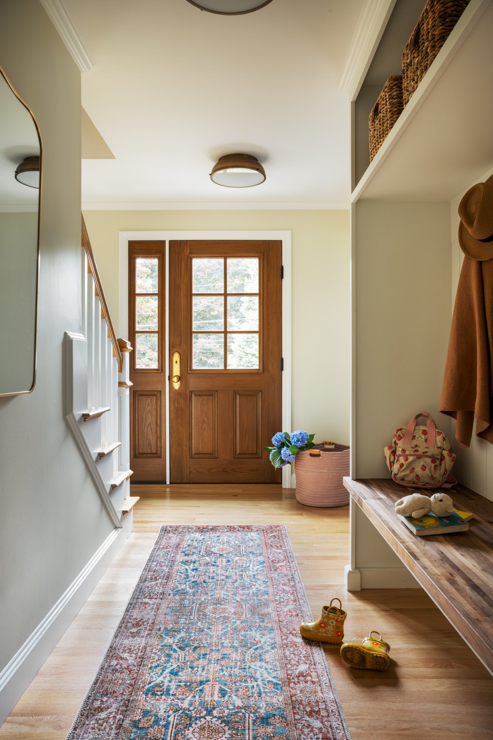 Front entry with a patterned runner, a wood door and a bench at the foot of the stairs