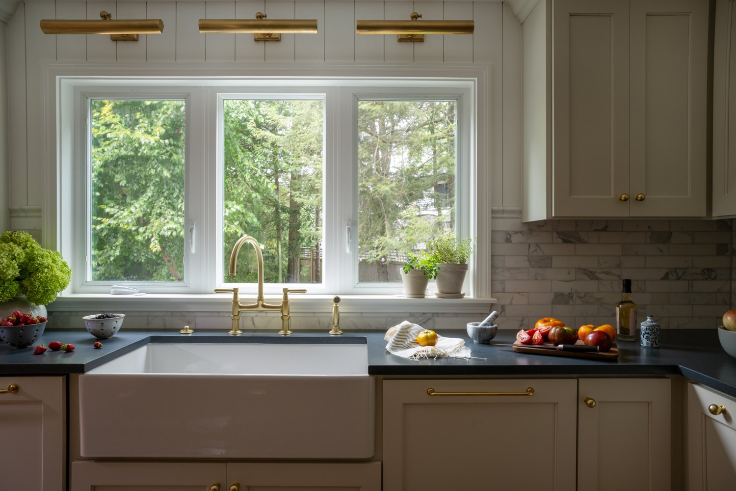 Farmhouse sink under a bank of windows with brass picture lights above the counter
