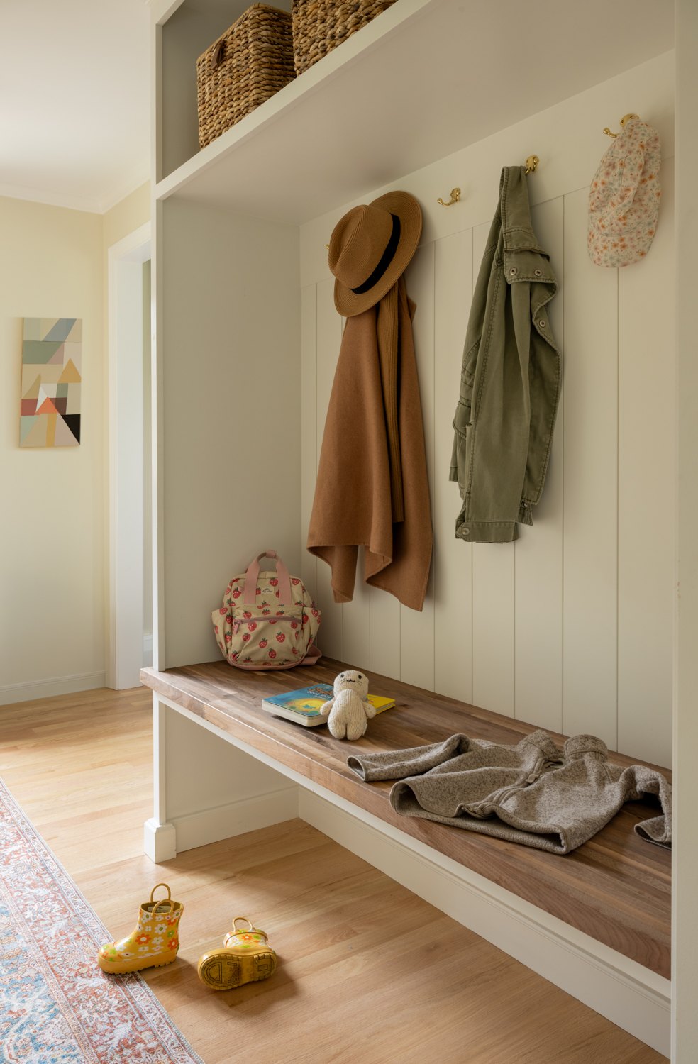 Mudroom bench with coat hooks, baskets overhead and shoes tucked underneath