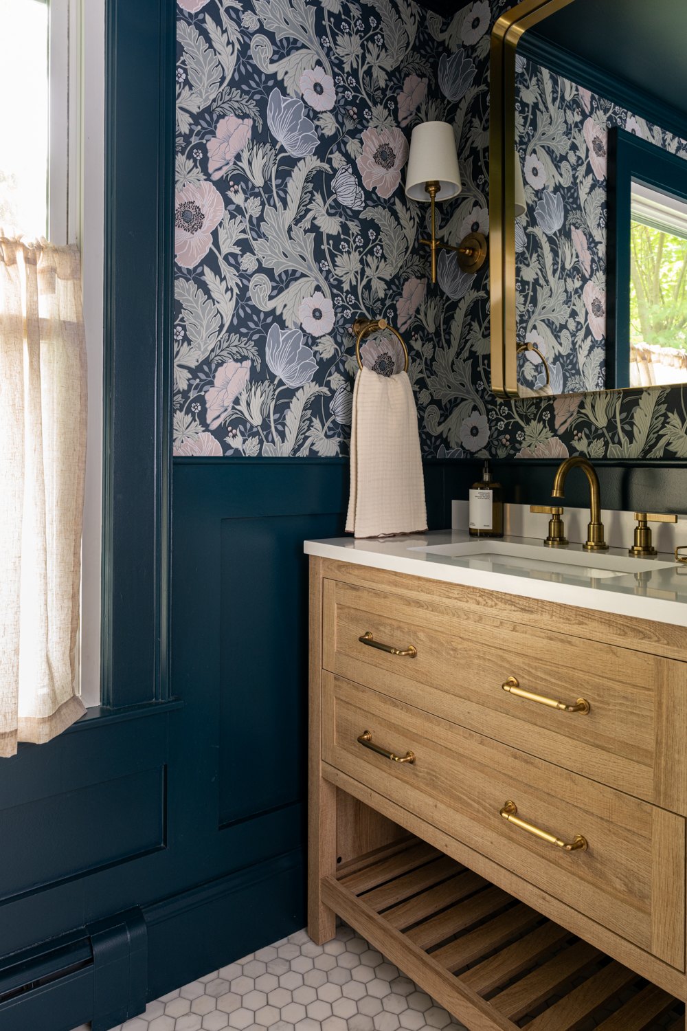 Powder room with floral wallpaper, navy wainscoting and a white oak vanity