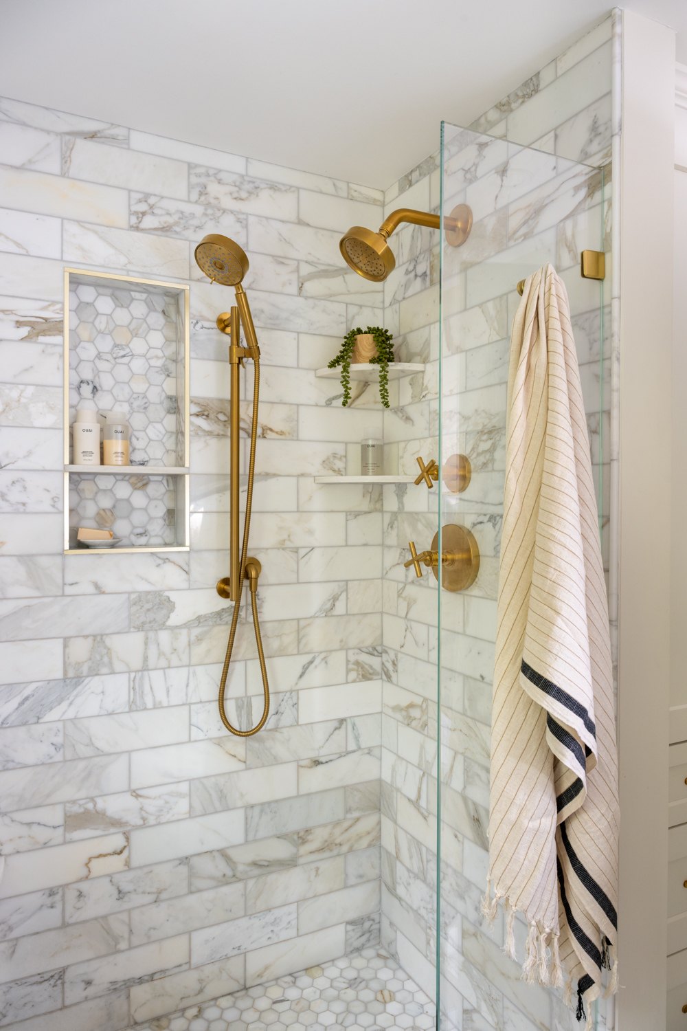 Walk-in shower tiled in marble with brass fittings and a recessed niche