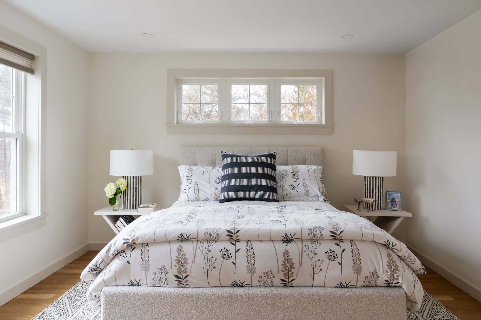 ADU bedroom with a made bed, striped pillow and windows above the headboard