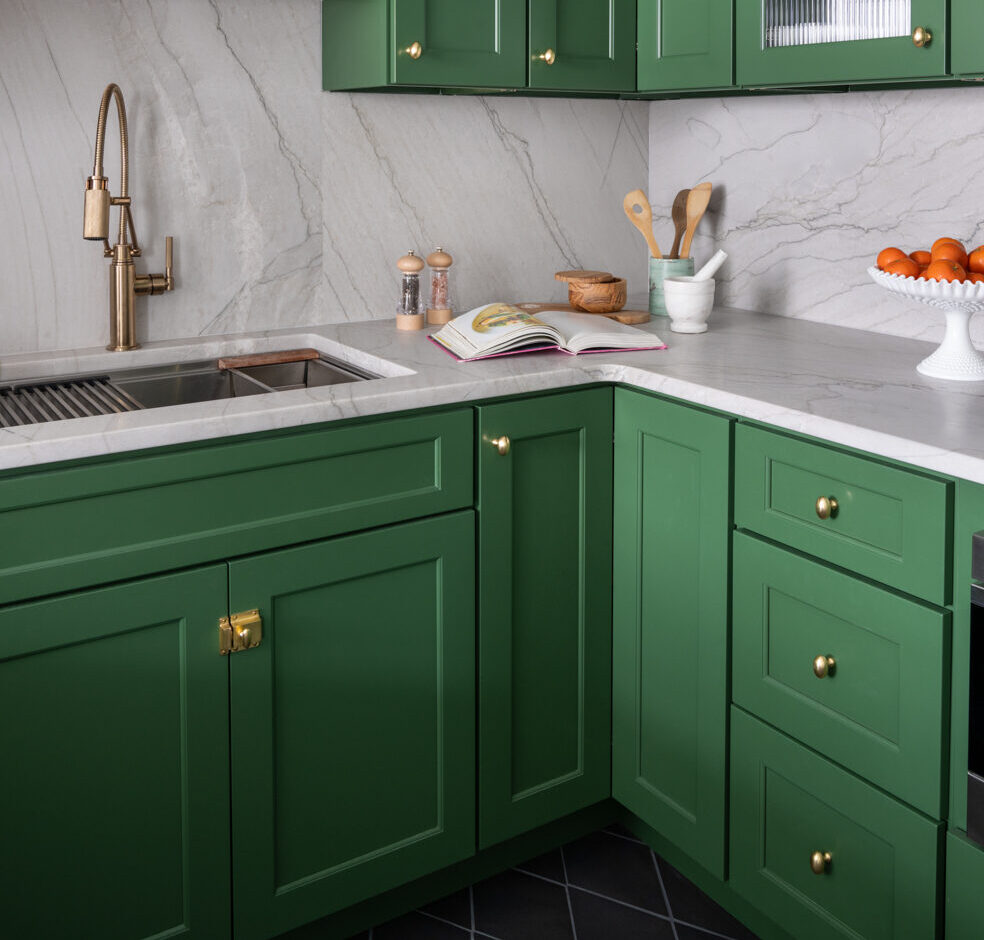 Green lower cabinets under a marble counter with a brass gooseneck faucet